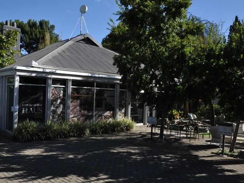 Front exterior view of a commercial property featuring a corrugated metal roof, large glass windows, and a paved entrance area with mature trees.