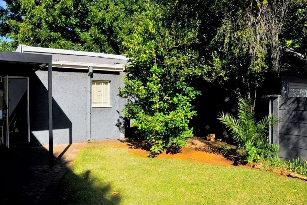 A view of the rear exterior featuring a small lawn, landscaped garden area, and a covered patio space adjacent to the building structure.