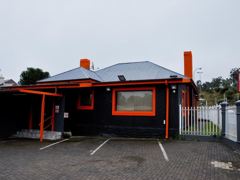 Commercial property exterior featuring a distinctive black and orange facade, corrugated metal roof, paved parking area, and secure perimeter fencing.