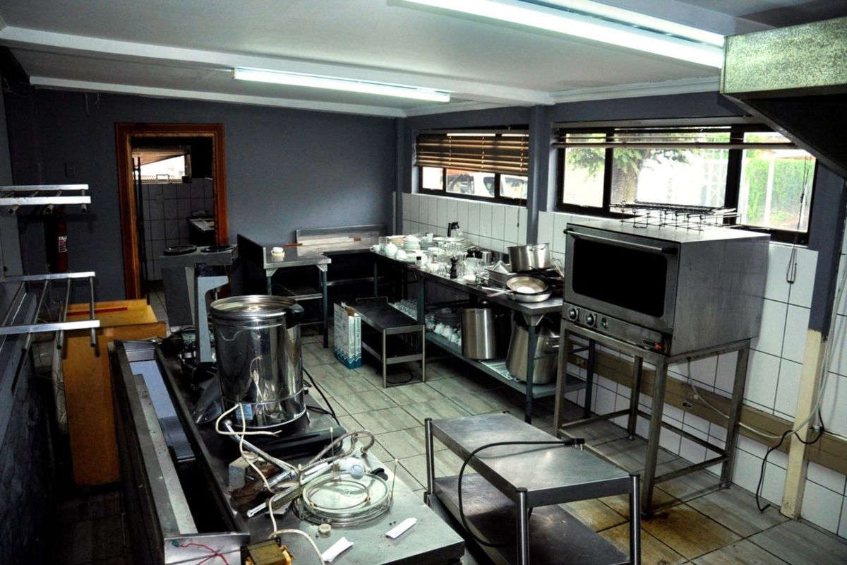 Commercial kitchen space featuring stainless steel prep surfaces, built-in oven, tiled splashbacks, and functional fluorescent lighting, suitable for professional food preparation.