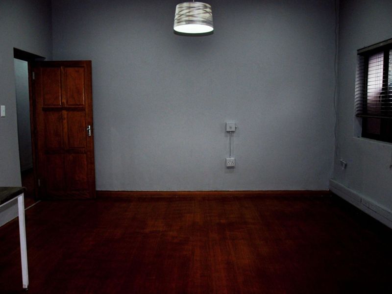 An empty office space featuring wooden flooring, a solid wood door, and a window with fitted blinds, suitable for a professional workspace.