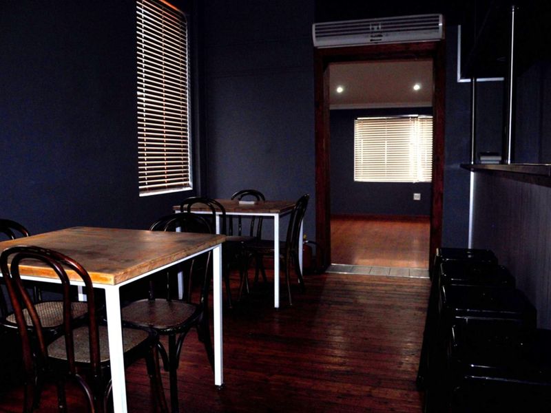 A commercial interior space featuring dark-painted walls, timber flooring, and a wall-mounted air conditioning unit, with an adjoining room visible through the doorway.