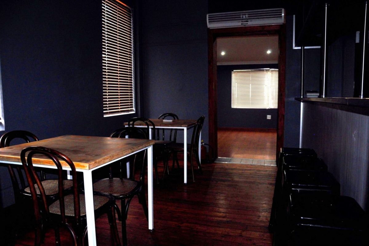 A commercial interior space featuring dark-painted walls, timber flooring, and a wall-mounted air conditioning unit, with an adjoining room visible through the doorway.