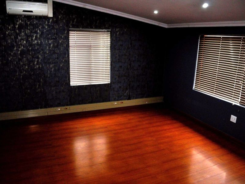 An empty office space featuring dark textured wallpaper, laminate wood flooring, recessed lighting, and a wall-mounted air conditioning unit.