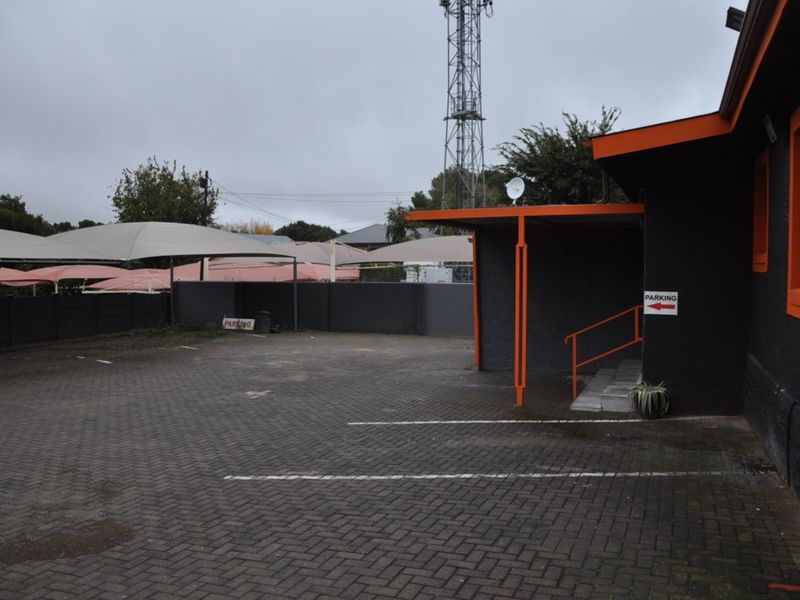 Commercial property exterior featuring a paved parking area with shade cloth carports and a covered building entrance.
