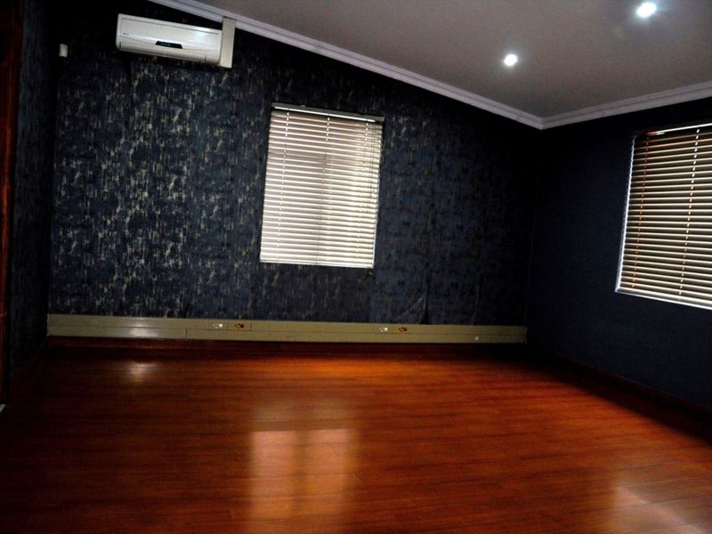 An empty office space featuring dark textured wallpaper, laminate wood flooring, recessed lighting, and a wall-mounted air conditioning unit.