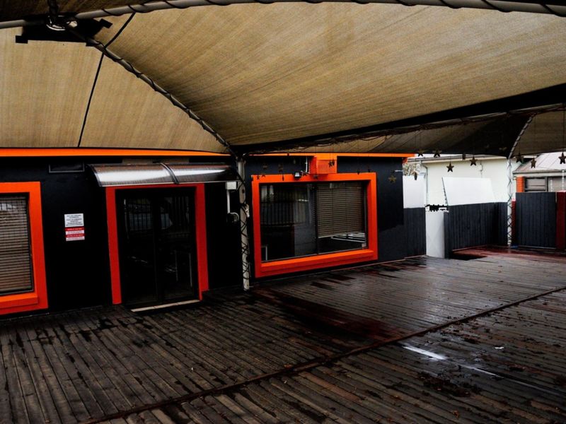 Covered outdoor patio area featuring timber decking, a large shade sail, and modern black and orange exterior wall accents.