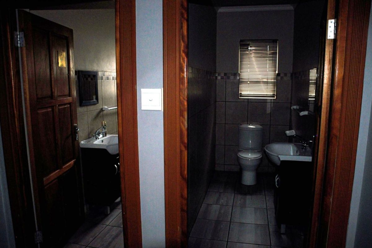 A functional bathroom featuring tiled walls and flooring, a vanity basin, and a toilet, with natural light provided by a window with venetian blinds.