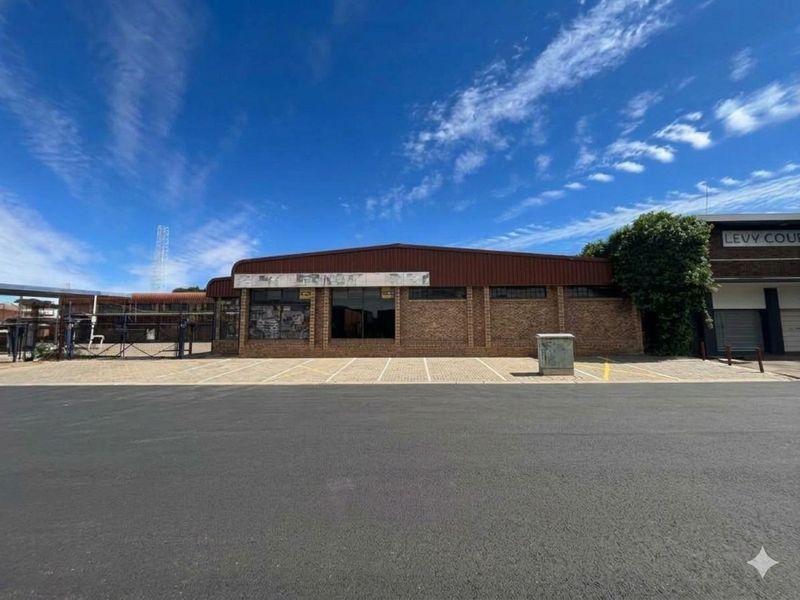 Front exterior view of a commercial property featuring a brick facade, metal roofing, and a paved parking area with large display windows.