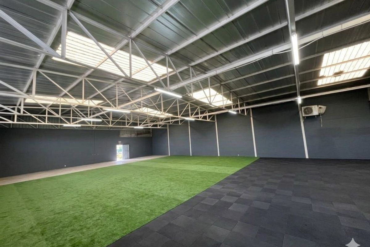 Spacious commercial sports facility featuring high exposed steel roof trusses, integrated skylights, and a combination of artificial turf and rubber flooring.