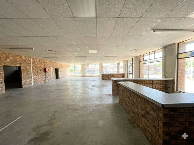Spacious open-plan commercial area featuring exposed brick walls, concrete flooring, and a built-in brick service counter, suitable for retail or office use.