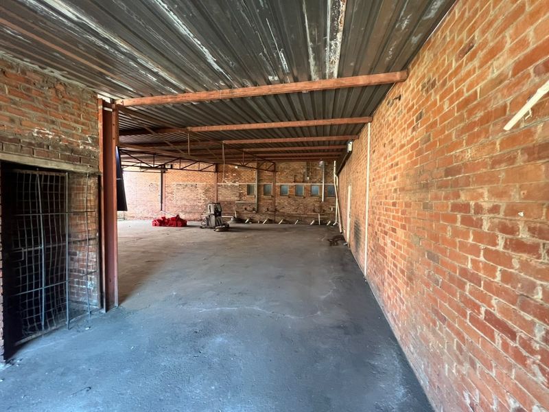 A large, open-plan industrial utility space featuring exposed brick walls, steel structural beams, and a corrugated metal ceiling with concrete flooring.