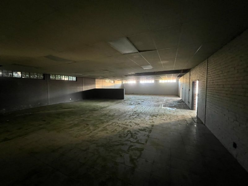 A large, vacant commercial open-plan space featuring exposed brick walls, tiled flooring, and a suspended ceiling, requiring significant refurbishment.