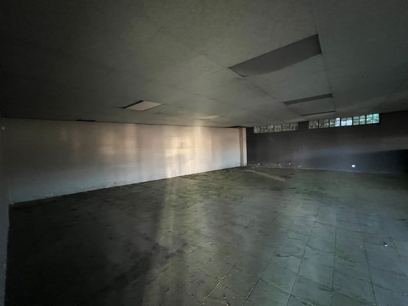 A large, vacant open-plan commercial space featuring tiled flooring, suspended ceiling with recessed lighting, and high-level glass block windows.