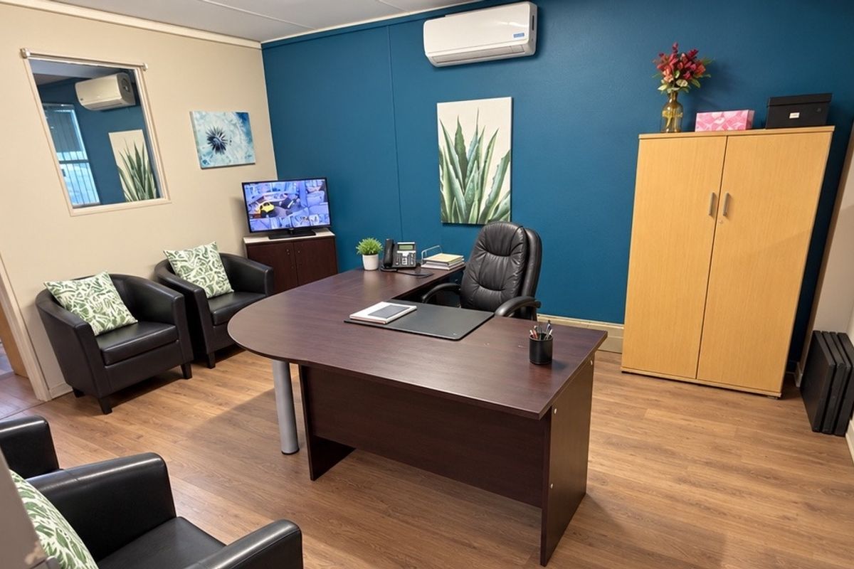 A well-maintained professional office space featuring laminate flooring, a split-system air conditioner, and an internal window providing natural light.