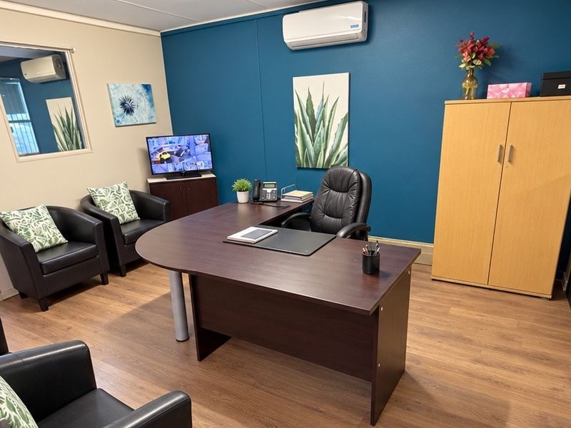 A well-maintained professional office space featuring laminate flooring, a split-system air conditioner, and an internal window providing natural light.