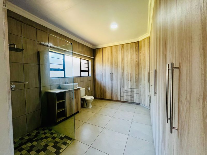 Modern bathroom featuring extensive built-in cabinetry, a glass-enclosed shower, vessel sink vanity, and neutral floor-to-ceiling tiling.