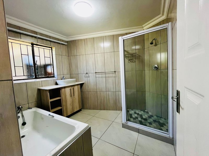 A clean, modern bathroom featuring a built-in vanity with a vessel sink, a separate shower enclosure, and a bathtub with neutral wall tiling.