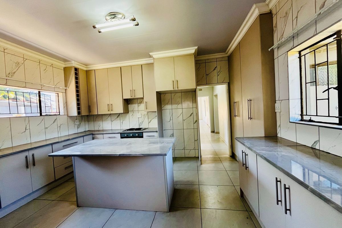 A spacious, modern kitchen featuring ample built-in cabinetry, a central island, marble-look countertops, and tiled finishes throughout.