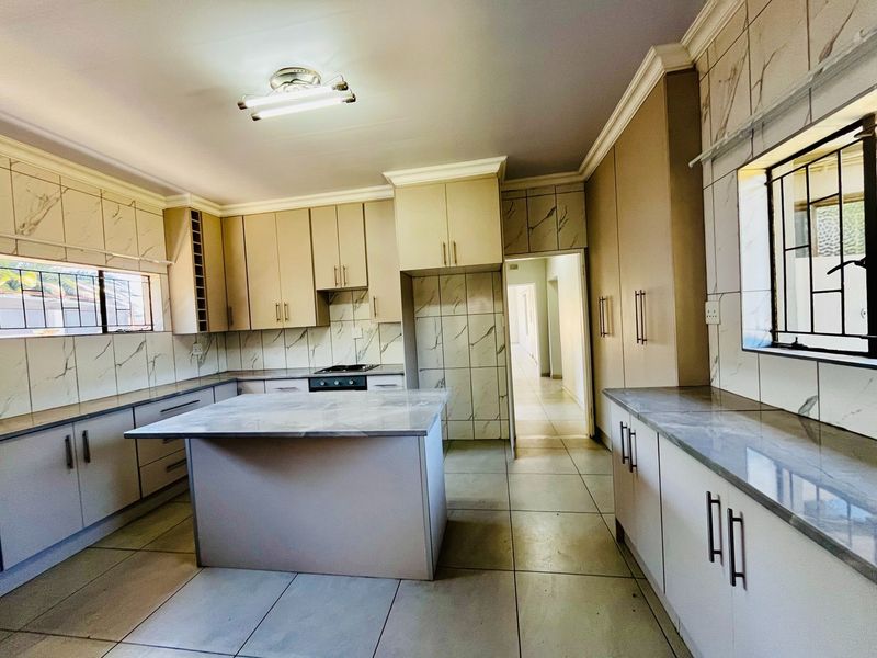 A spacious, modern kitchen featuring ample built-in cabinetry, a central island, marble-look countertops, and tiled finishes throughout.