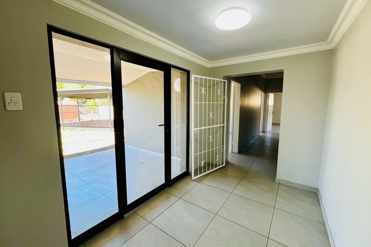 A bright, empty living area featuring neutral tiled flooring, modern sliding glass doors leading to the patio, and a secure entrance gate.