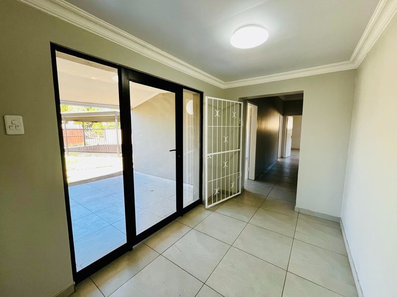 A bright, empty living area featuring neutral tiled flooring, modern sliding glass doors leading to the patio, and a secure entrance gate.