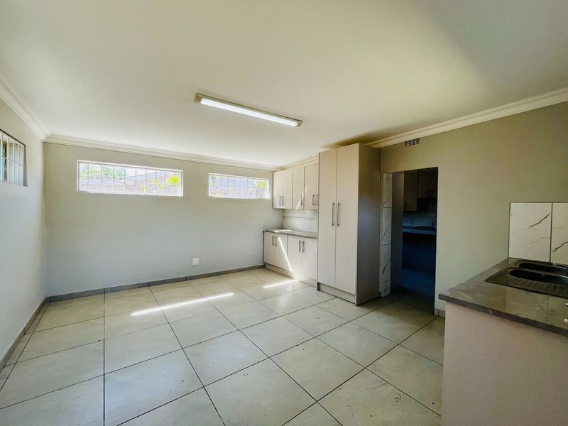 A spacious, empty kitchen featuring neutral built-in cabinetry, tiled flooring, and high-level windows, offering a clean canvas for potential updates.