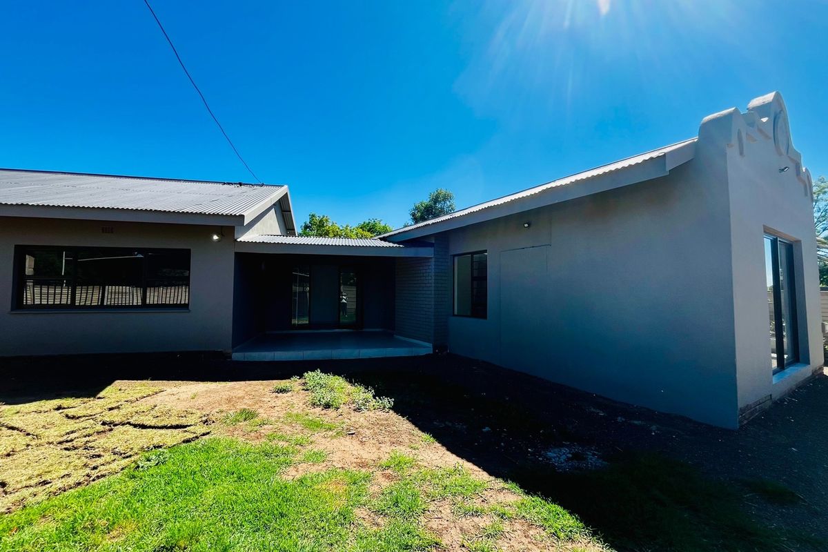 Rear view of the house featuring a covered patio area, modern grey exterior walls, and a corrugated metal roof with a lawn area.