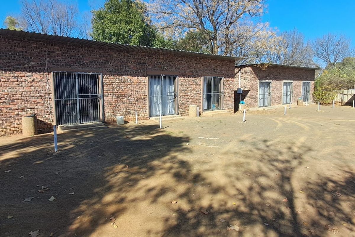Exterior view of a row of brick units featuring sliding doors with security gates and a large unpaved yard area.