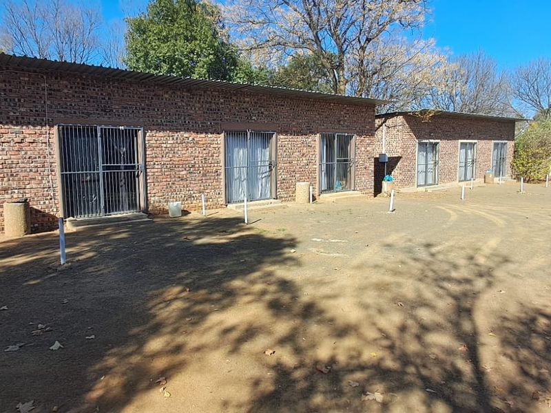Exterior view of a row of brick units featuring sliding doors with security gates and a large unpaved yard area.