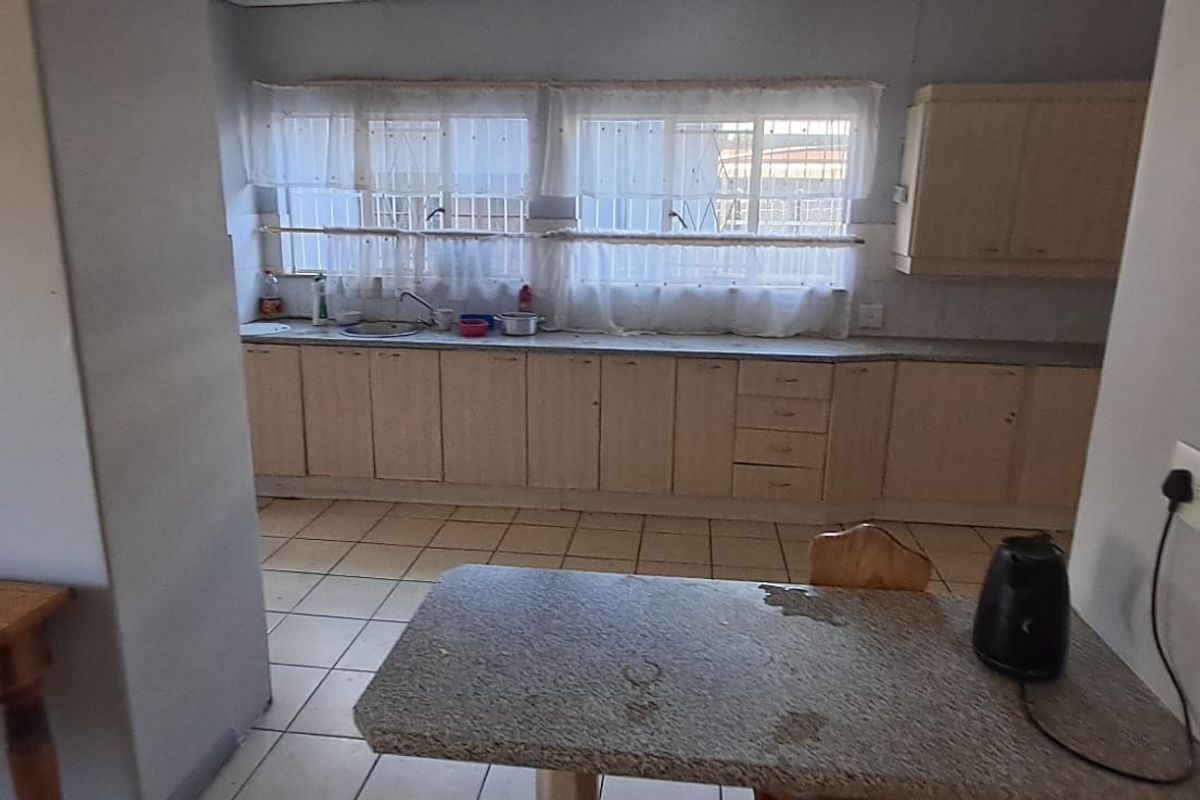 A functional kitchen featuring extensive built-in cabinetry, laminate countertops, tiled flooring, and large windows with security bars, offering a practical layout for daily use.