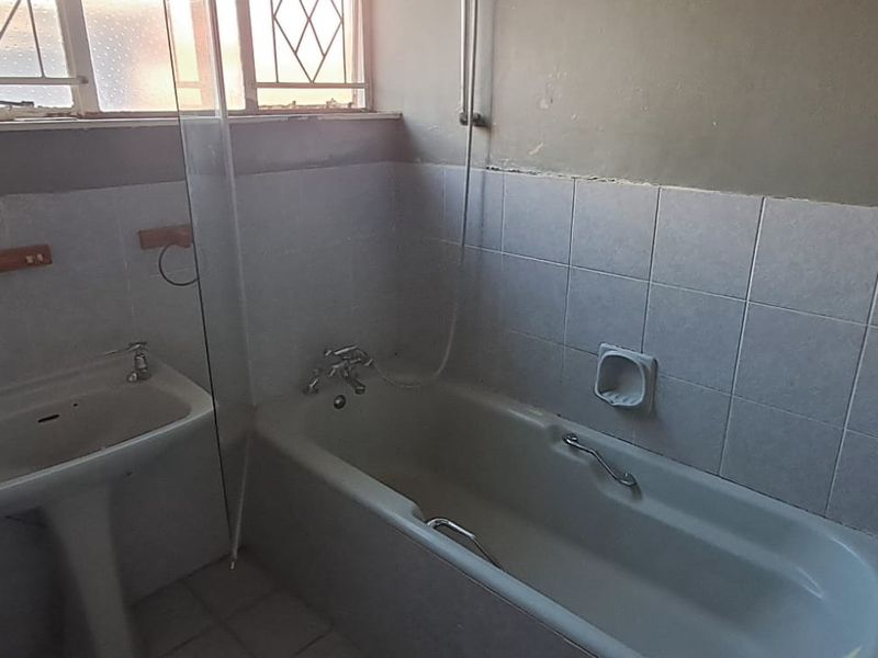 A dated bathroom featuring a pedestal basin, bathtub with shower screen, and tiled walls, requiring cosmetic updates to improve its condition.