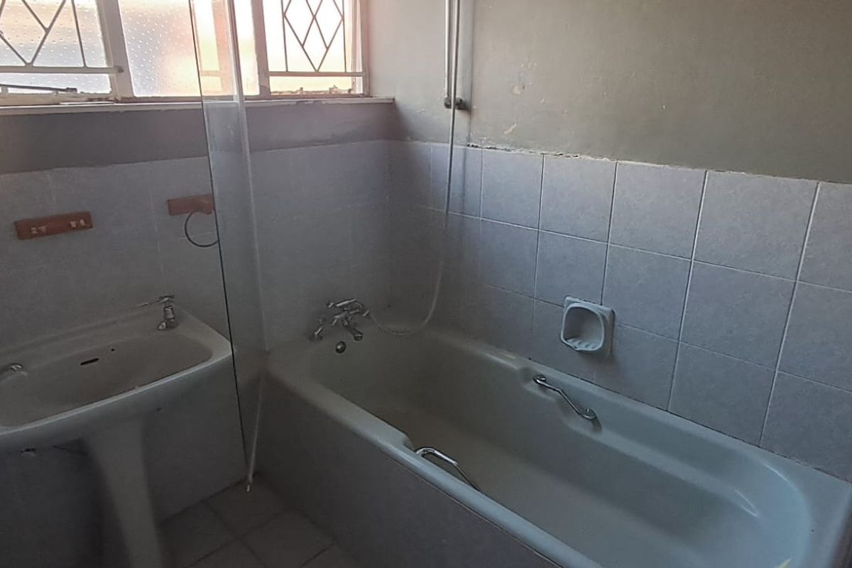 A dated bathroom featuring a pedestal basin, bathtub with shower screen, and tiled walls, requiring cosmetic updates to improve its condition.