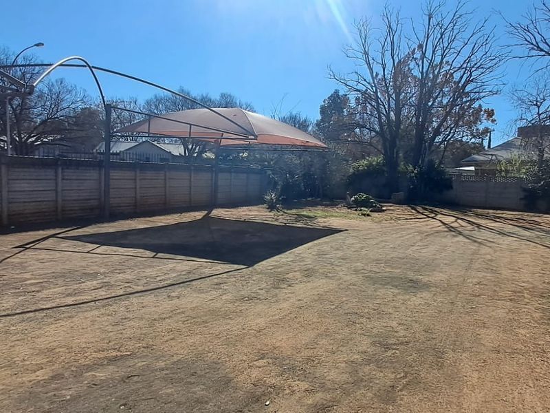 Spacious rear yard featuring a precast concrete boundary wall, a shade cloth carport structure, and a paved walkway along the building exterior.