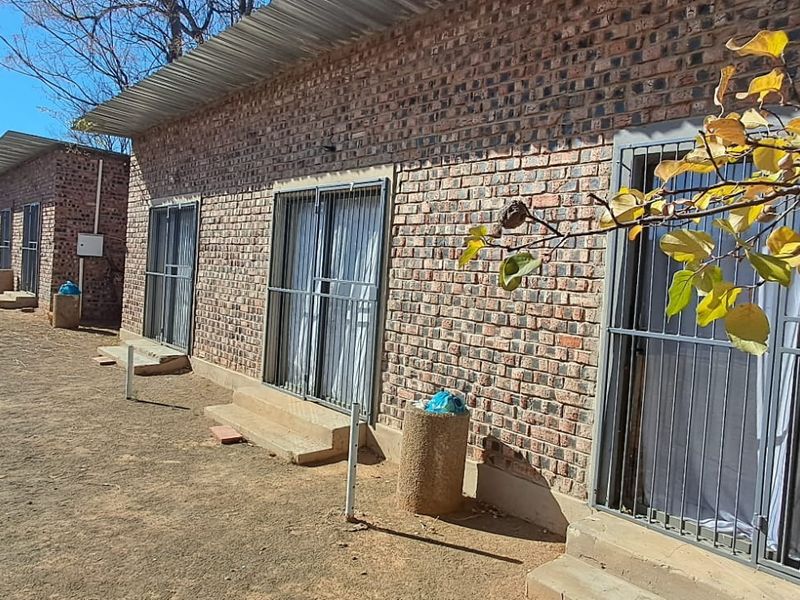 Rear view of a brick residential building featuring multiple sliding glass doors with security gates and a corrugated metal roof.