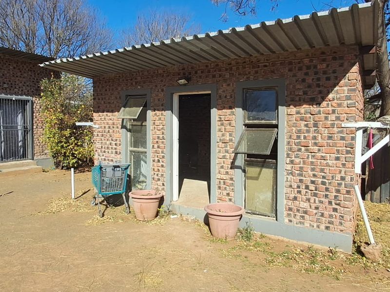 A view of a detached brick outbuilding with a corrugated metal roof, featuring top-hung windows and security bars in a rear yard setting.