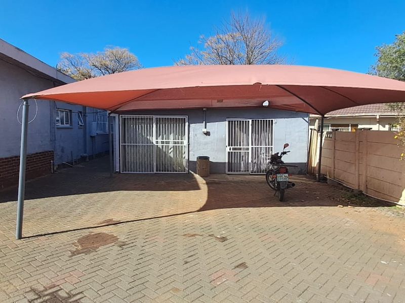 Rear exterior view featuring a paved driveway, a large shade sail structure, and secure sliding door access to the main building.