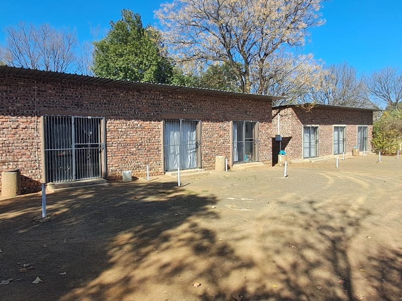 Rear view of a face brick building featuring multiple sliding door entrances with security gates and a corrugated metal roof.