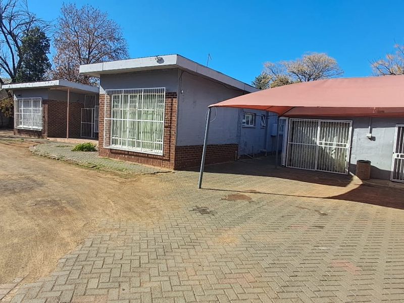 Front exterior view of the property featuring a paved driveway, shade cloth carport, and multiple building sections with security bars on windows.