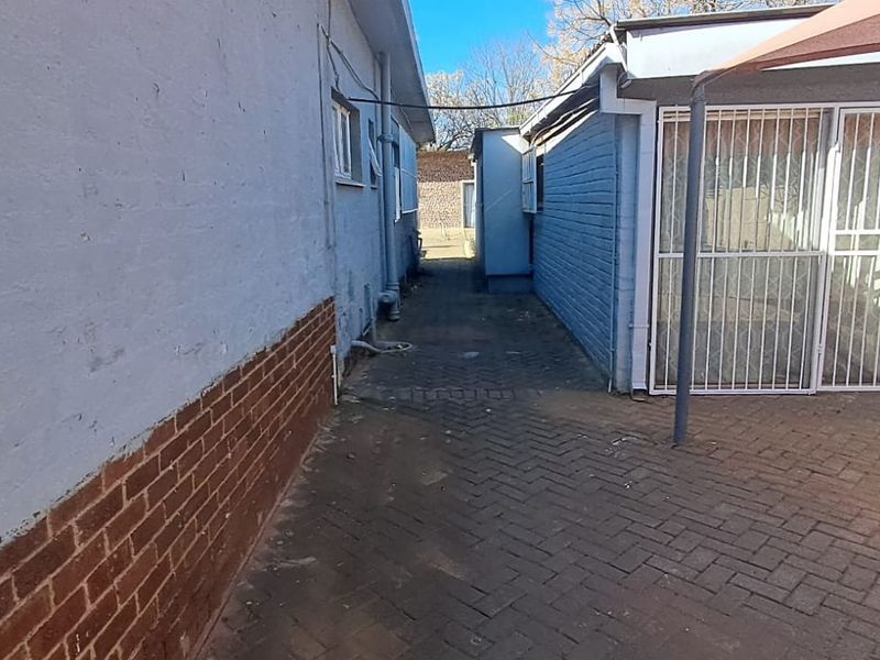 A narrow exterior side passage featuring brick paving, painted brick walls, and a security gate leading to the rear of the property.