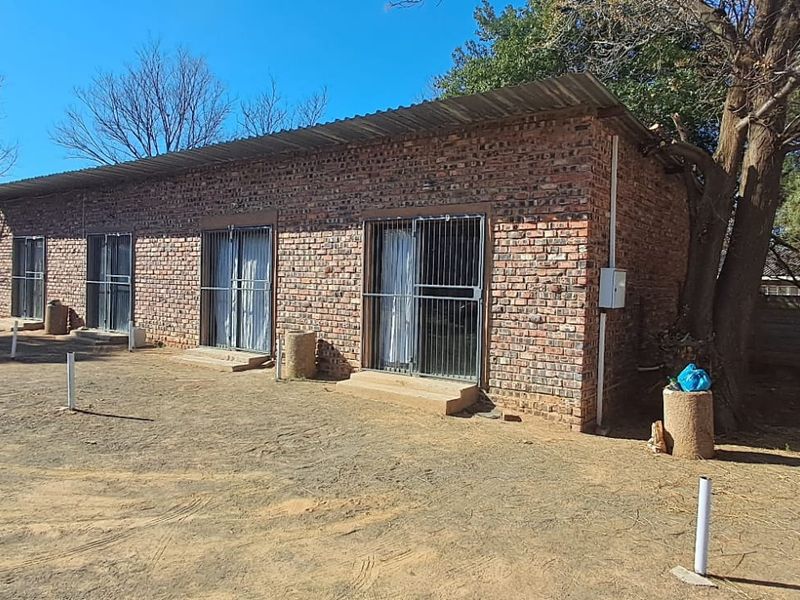 Rear view of a face brick building featuring multiple sliding door entrances with security gates and a corrugated metal roof.