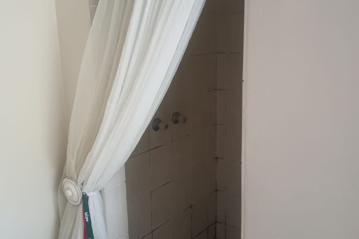 A basic shower enclosure featuring tiled walls and a standard mixer, currently showing signs of wear and requiring maintenance or renovation.