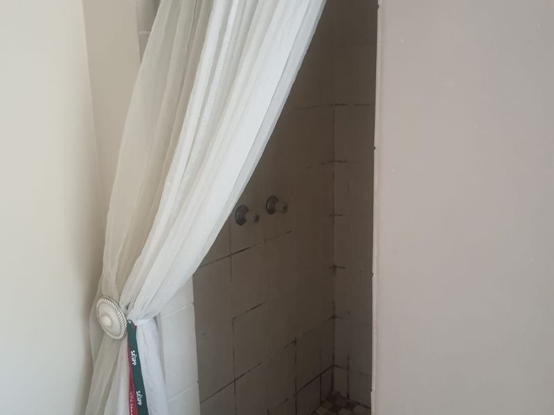 A basic shower enclosure featuring tiled walls and a standard mixer, currently showing signs of wear and requiring maintenance or renovation.