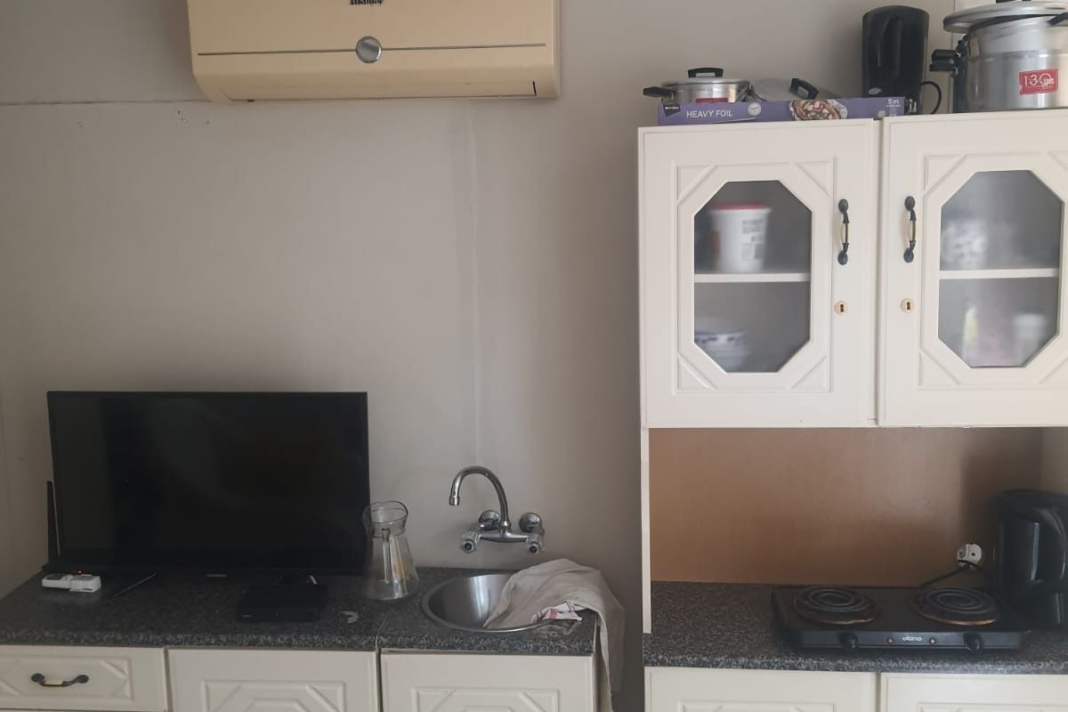 A compact kitchen area featuring built-in cabinetry, a stainless steel sink, and an electric hob, with a wall-mounted air conditioning unit above.