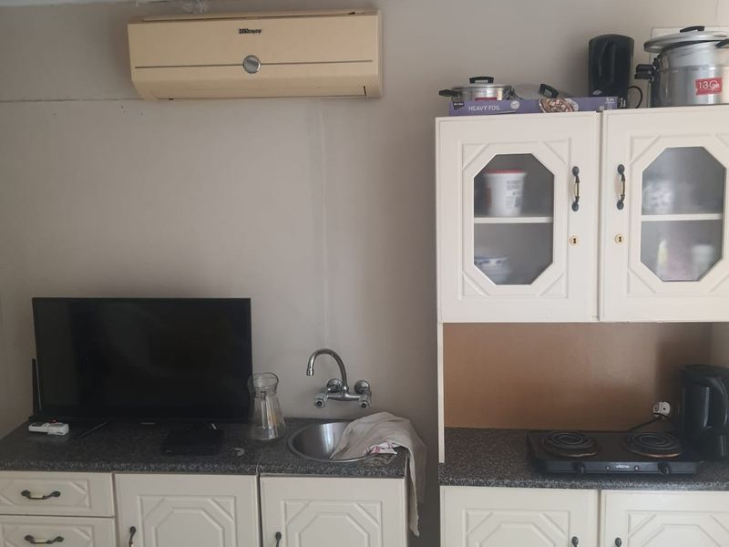 A compact kitchen area featuring built-in cabinetry, a stainless steel sink, and an electric hob, with a wall-mounted air conditioning unit above.