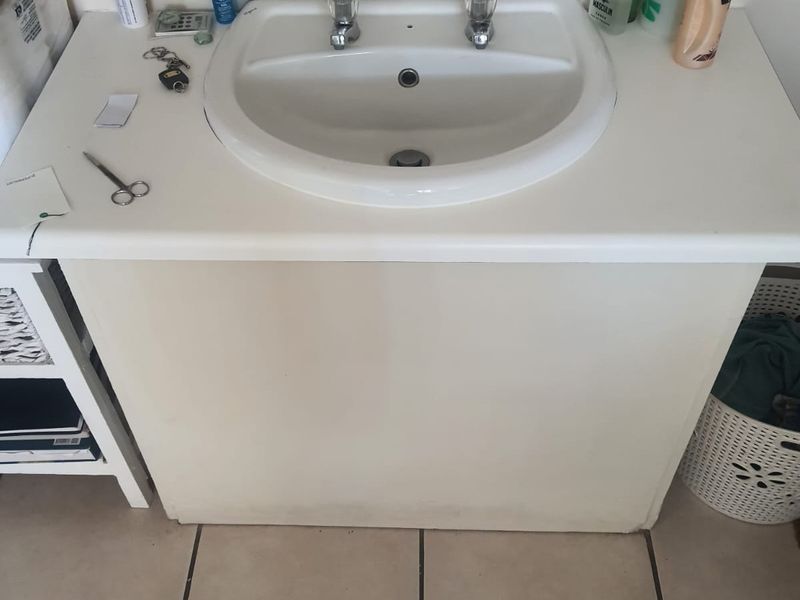 A bathroom vanity unit featuring a white ceramic basin and dual taps, set against tiled flooring.