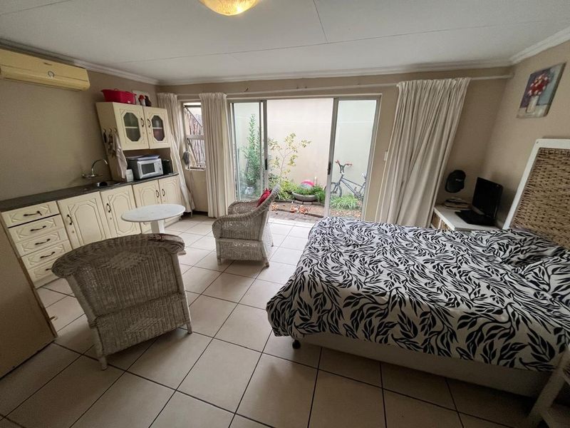 Open-plan studio apartment featuring a kitchenette with built-in cabinetry, tiled flooring, and sliding glass doors providing access to a private outdoor courtyard area.