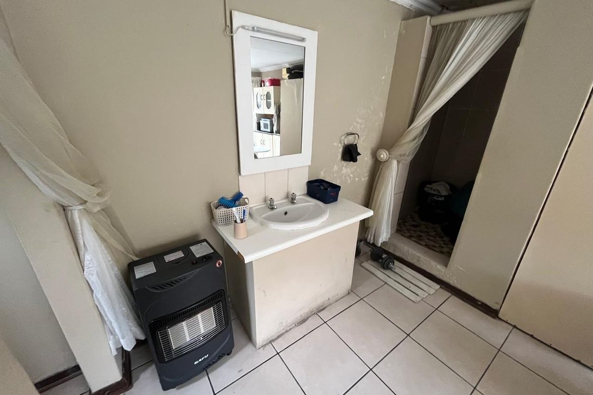 A dated bathroom featuring a vanity basin, wall-mounted mirror, and a shower enclosure with tiled flooring, requiring cosmetic updates and repairs to wall finishes.