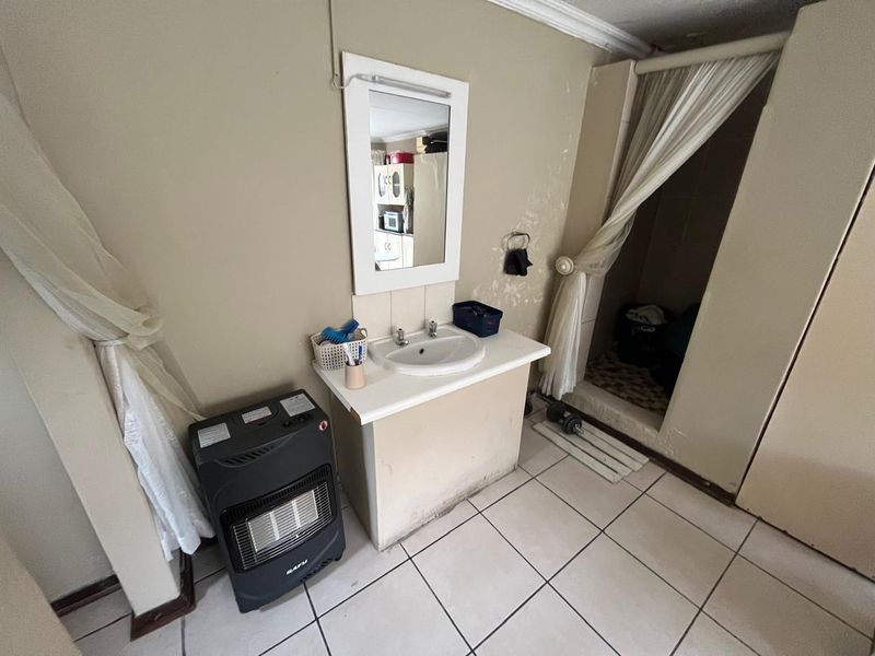 A dated bathroom featuring a vanity basin, wall-mounted mirror, and a shower enclosure with tiled flooring, requiring cosmetic updates and repairs to wall finishes.