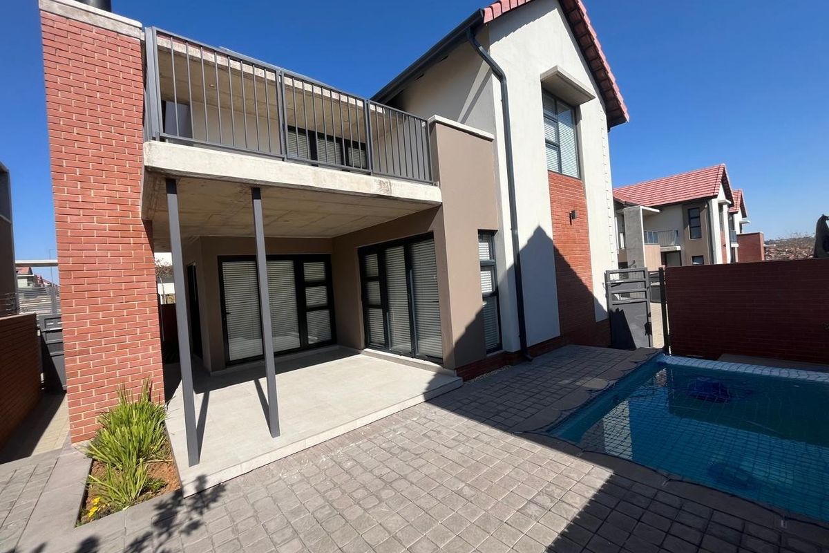 Rear view of the townhouse featuring a covered patio, an upper-level balcony with metal railings, and a private swimming pool set in a paved courtyard.